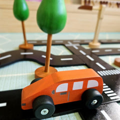 QToys - Coloured Wooden Cars - Wooden toy car on a road with green trees in the background