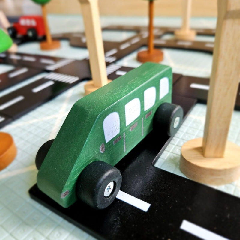 QToys - Coloured Wooden Cars - Green toy bus on a wooden road with other toys in the background