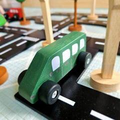 QToys - Coloured Wooden Cars - Green toy bus on a wooden road with other toys in the background